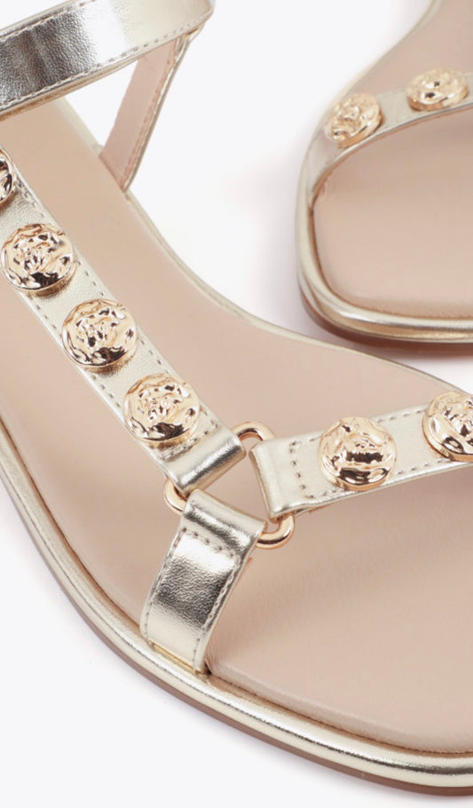 Dettaglio borchie tonde dorate su cinturino a T sandalo flat oro Lola Casademunt